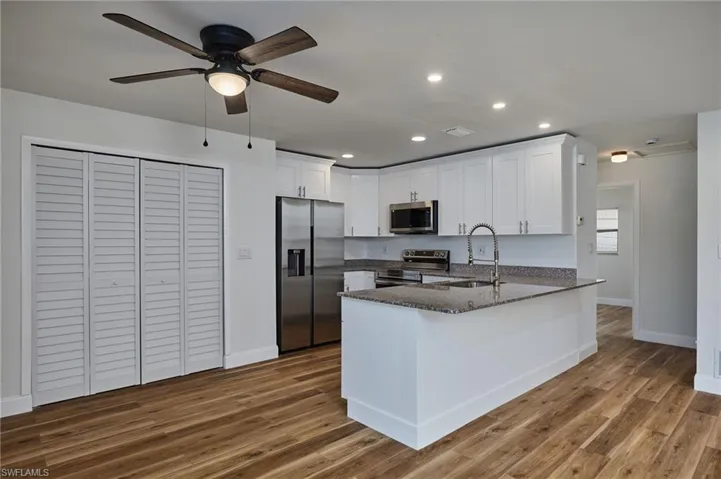 Kitchen with appliances with stainless steel finishes, a peninsula, white cabinetry, dark stone counters, and recessed lighting