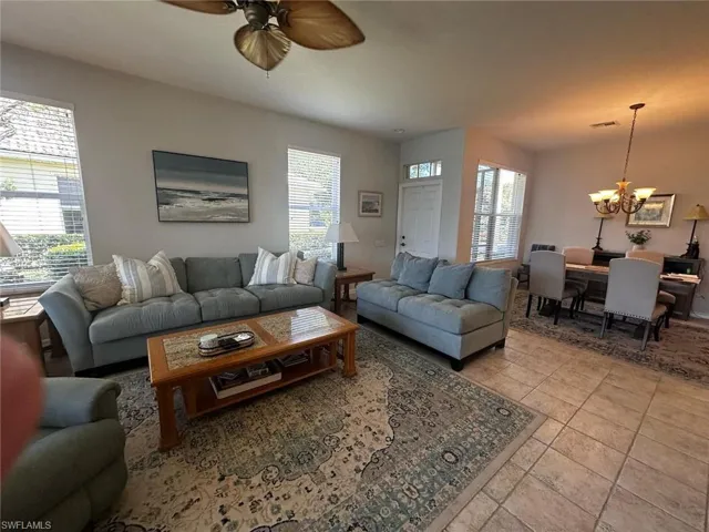 Living area with light tile patterned flooring, ceiling fan with notable chandelier, and plenty of natural light