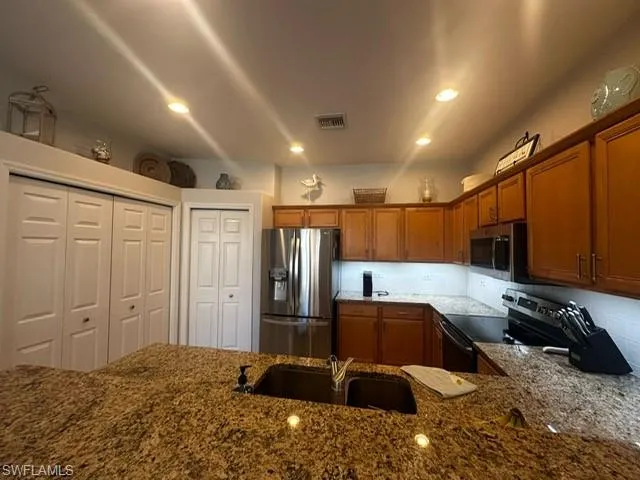 Kitchen with a sink, dark stone counters, visible vents, brown cabinets, and appliances with stainless steel finishes