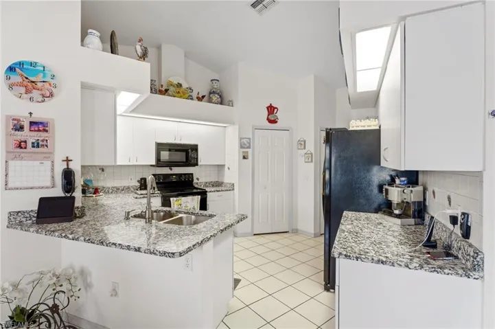 Kitchen featuring decorative backsplash, black appliances, a peninsula, white cabinetry, and light tile patterned floors