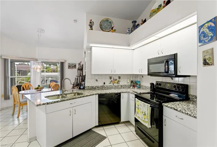Kitchen with black appliances, a peninsula, decorative backsplash, and white cabinets