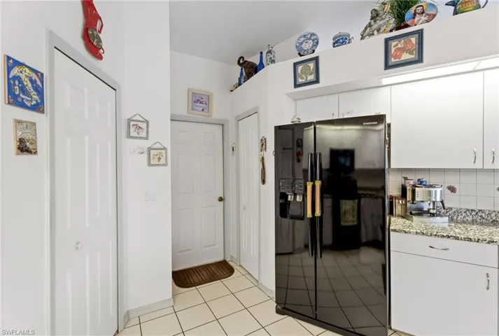 Kitchen with black refrigerator with ice dispenser, white cabinetry, light tile patterned floors, decorative backsplash, and light stone countertops