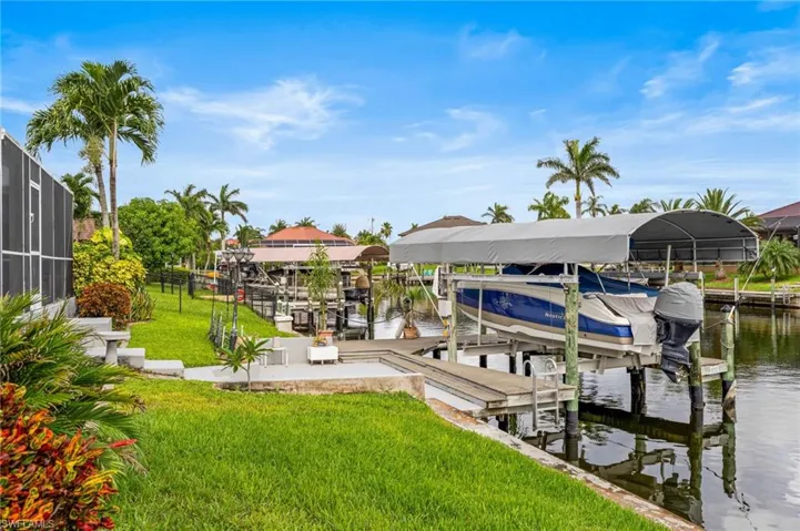 Dock with boat lift, a water view, and a lawn