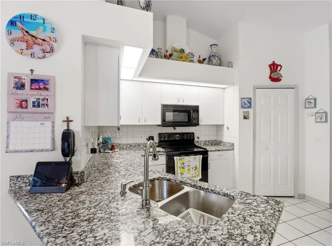 Kitchen featuring black appliances, light stone countertops, decorative backsplash, white cabinetry, and light tile patterned flooring