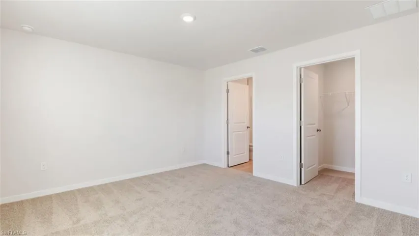 Model home. Unfurnished bedroom featuring light carpet and a walk in closet