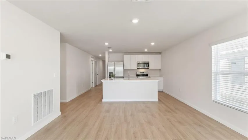 Model home. Kitchen with light countertops, an island with sink, white cabinetry, stainless steel appliances, and light wood-style flooring