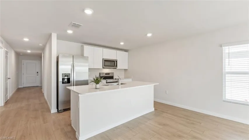 Model home. Kitchen with stainless steel appliances, a center island with sink, white cabinetry, light wood-type flooring, and recessed lighting