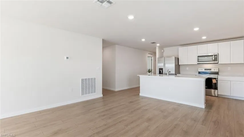 Model home. Kitchen with stainless steel appliances, white cabinets, a center island with sink, light wood-type flooring, and recessed lighting