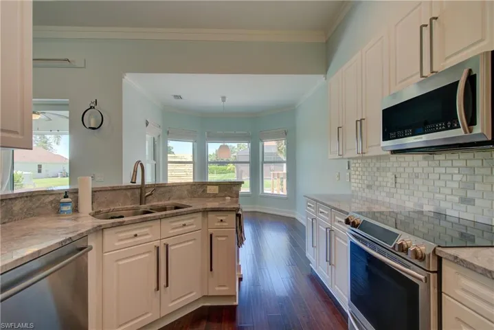 Kitchen featuring appliances with stainless steel finishes, light stone countertops, white cabinetry, ornamental molding, and decorative backsplash