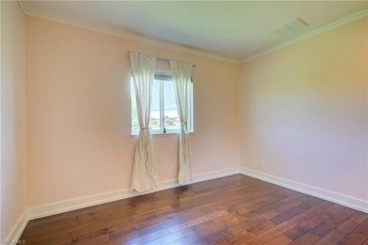 Empty room featuring crown molding and dark wood-type flooring