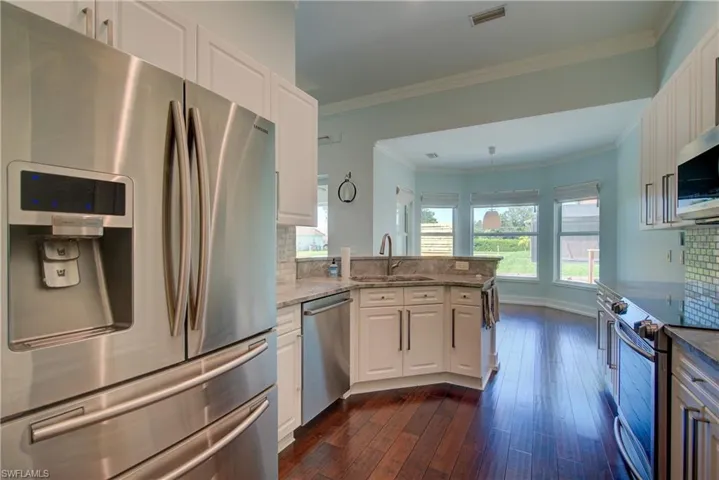Kitchen with appliances with stainless steel finishes, backsplash, white cabinetry, crown molding, and light stone countertops
