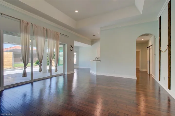 Unfurnished living room featuring a tray ceiling, dark wood finished floors, crown molding, arched walkways, and recessed lighting