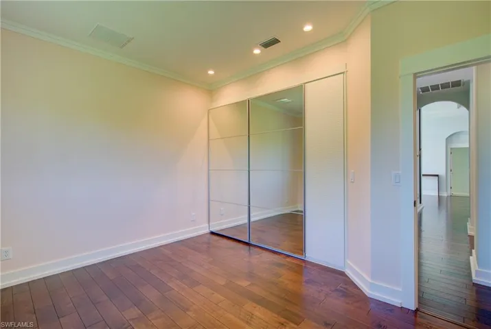 Unfurnished bedroom featuring arched walkways, dark wood-style flooring, crown molding, a closet, and recessed lighting