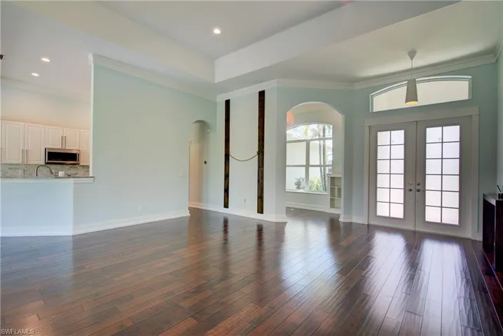 Unfurnished living room featuring arched walkways, ornamental molding, french doors, dark wood finished floors, and recessed lighting