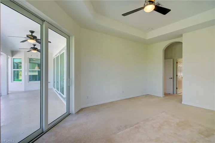 Unfurnished room with a ceiling fan, light colored carpet, a raised ceiling, and arched walkways