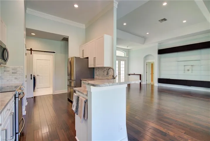 Kitchen featuring white cabinets, a barn door, decorative backsplash, open floor plan, and recessed lighting