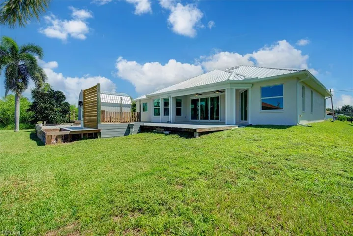 Back of house with a lawn, a wooden deck, a metal roof, and a ceiling fan