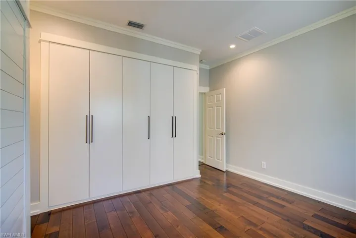 Unfurnished bedroom with a closet, crown molding, dark wood finished floors, and recessed lighting