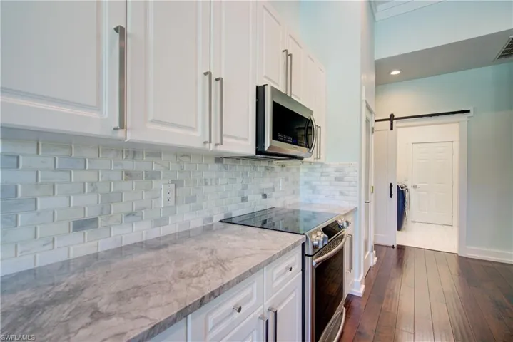 Kitchen with appliances with stainless steel finishes, white cabinets, tasteful backsplash, a barn door, and dark wood finished floors
