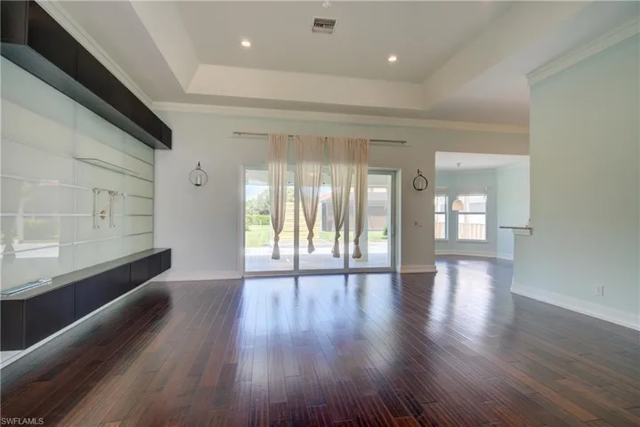 Unfurnished living room with a tray ceiling, dark wood-style flooring, ornamental molding, and recessed lighting