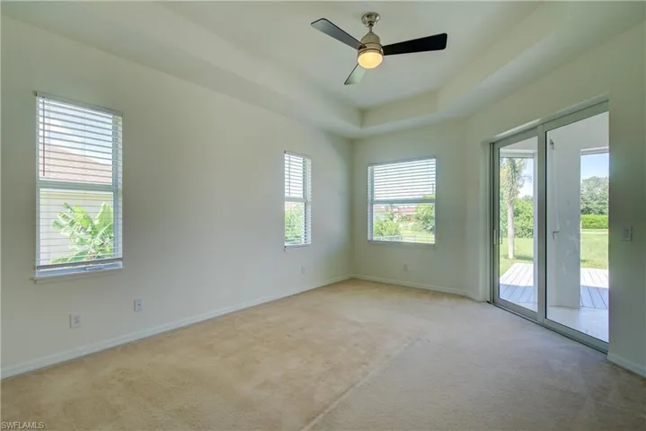 Carpeted empty room with healthy amount of natural light, a tray ceiling, and a ceiling fan