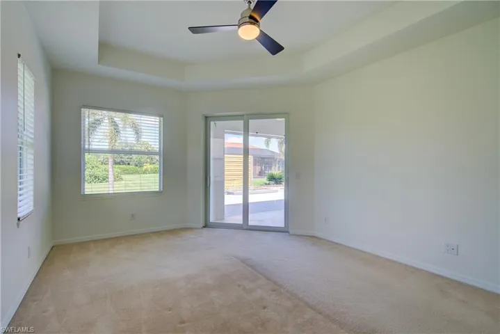 Empty room featuring a tray ceiling, light colored carpet, and ceiling fan