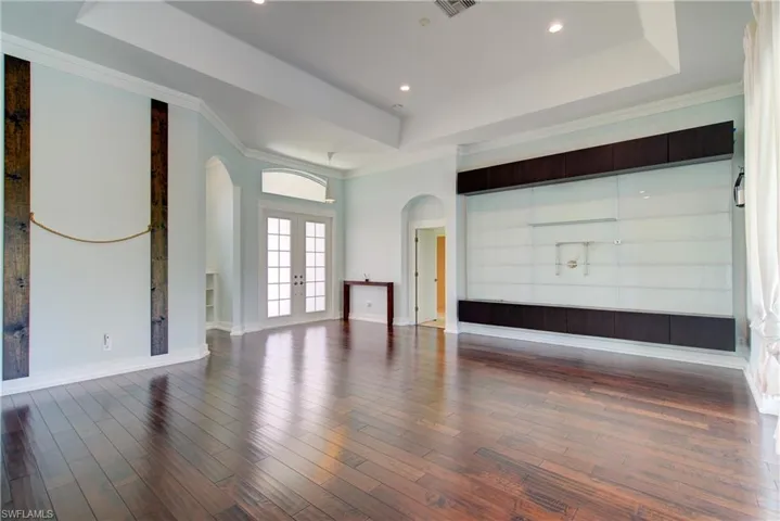 Unfurnished living room featuring arched walkways, a raised ceiling, french doors, ornamental molding, and dark wood finished floors