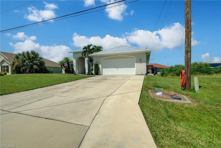 Ranch-style home featuring a front yard, an attached garage, concrete driveway, and a metal roof