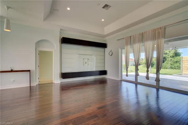 Unfurnished living room with a tray ceiling, dark wood-style flooring, arched walkways, and recessed lighting