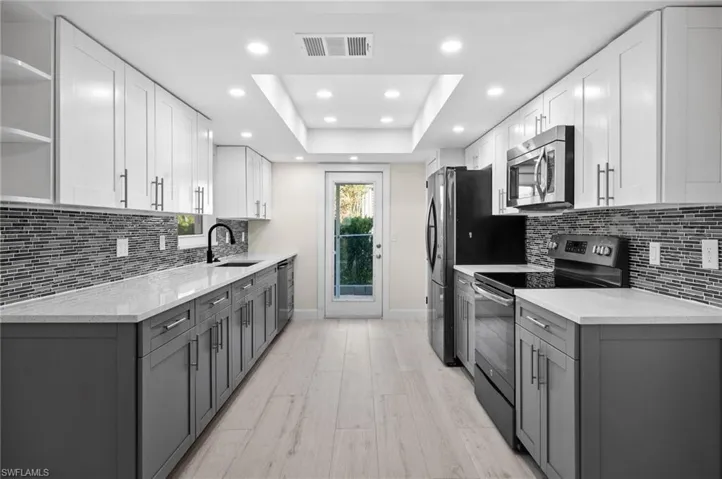 Kitchen with gray cabinets, visible vents, a raised ceiling, appliances with stainless steel finishes, and a sink