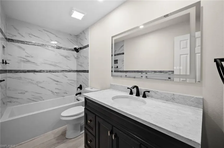 Bathroom featuring toilet, shower / bath combination, wood finished floors, and vanity