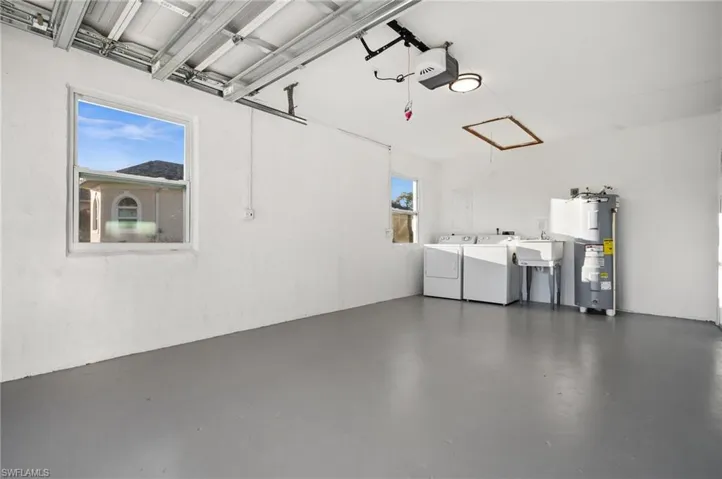 Garage with a garage door opener, water heater, independent washer and dryer, and a sink