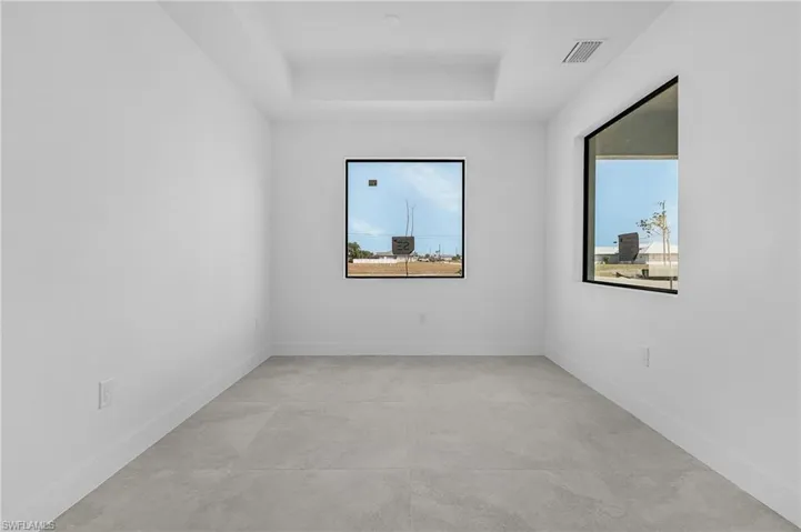 Empty room featuring baseboards, a tray ceiling, visible vents, and plenty of natural light
