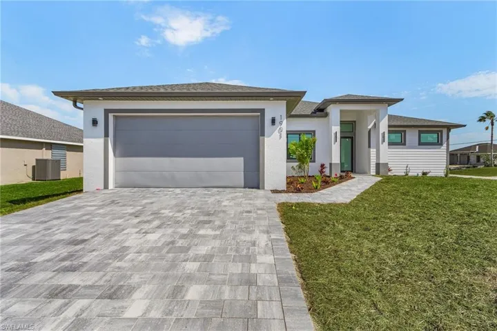 Prairie-style house featuring cooling unit, stucco siding, a front lawn, decorative driveway, and a garage