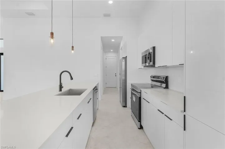 Kitchen with white cabinetry, light countertops, a sink, modern cabinets, and appliances with stainless steel finishes