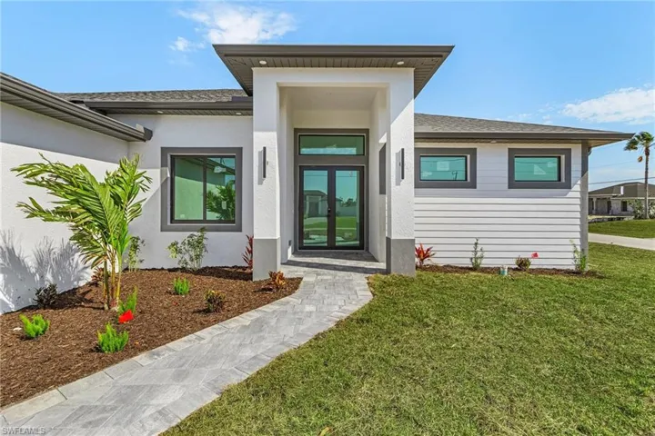 Property entrance with a shingled roof, stucco siding, french doors, and a yard