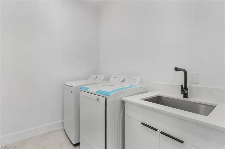 Clothes washing area featuring washer and clothes dryer, cabinet space, baseboards, and a sink