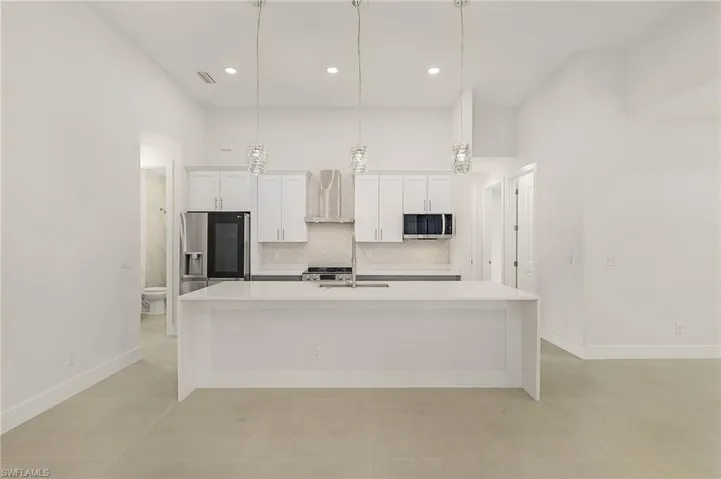 Kitchen featuring appliances with stainless steel finishes, decorative light fixtures, a center island with sink, and wall chimney exhaust hood