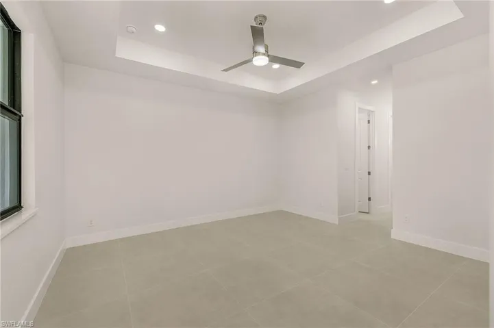 Tiled empty room with ceiling fan and a raised ceiling