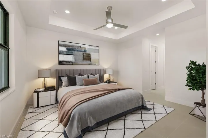 Bedroom with light tile patterned flooring, ceiling fan, and a raised ceiling