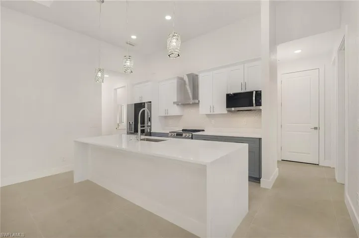 Kitchen featuring tasteful backsplash, wall chimney range hood, an island with sink, hanging light fixtures, and appliances with stainless steel finishes