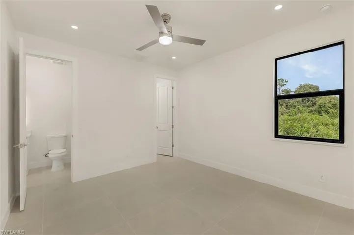 Unfurnished bedroom featuring ensuite bath, light tile patterned floors, and ceiling fan
