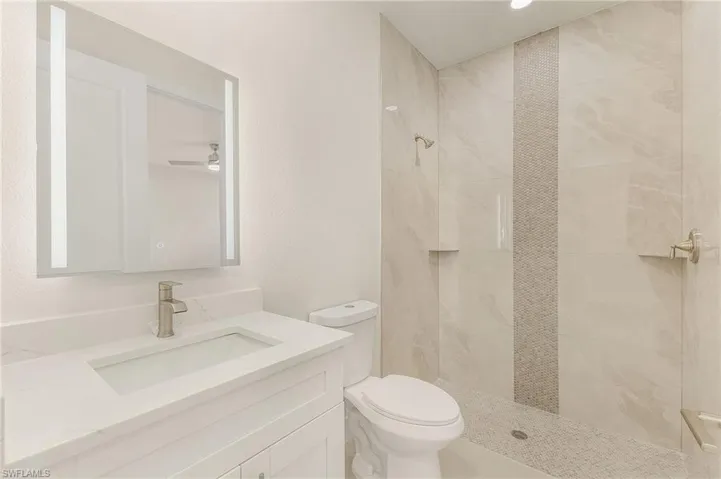 Bathroom with tiled shower, vanity, ceiling fan, and toilet