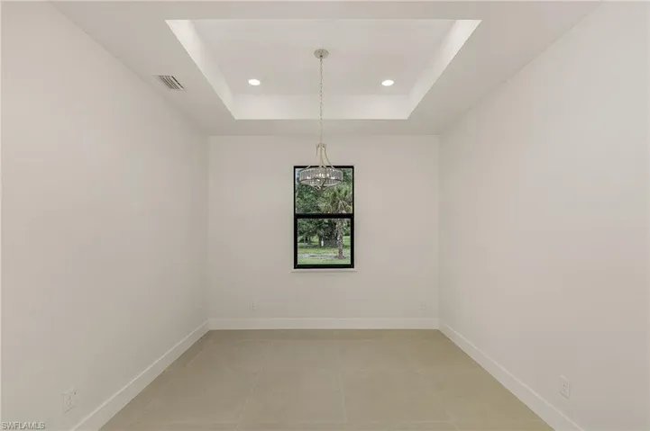 Empty room featuring tile patterned floors, a raised ceiling, and a notable chandelier