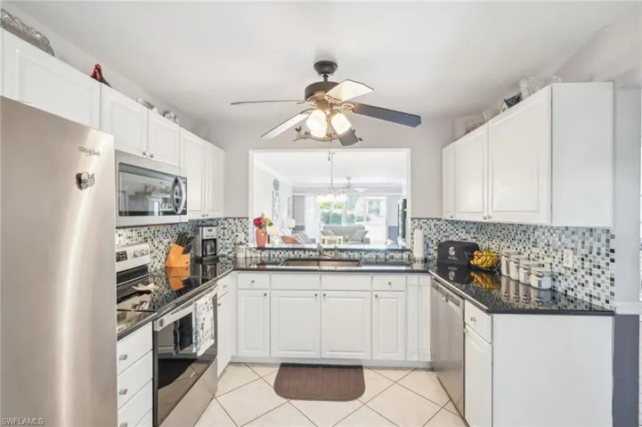 Kitchen with sink, light tile patterned flooring, stainless steel appliances, white cabinets, and decorative backsplash