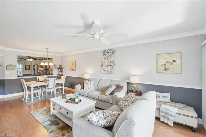 Living room with ornamental molding, light hardwood / wood-style flooring, and ceiling fan with notable chandelier