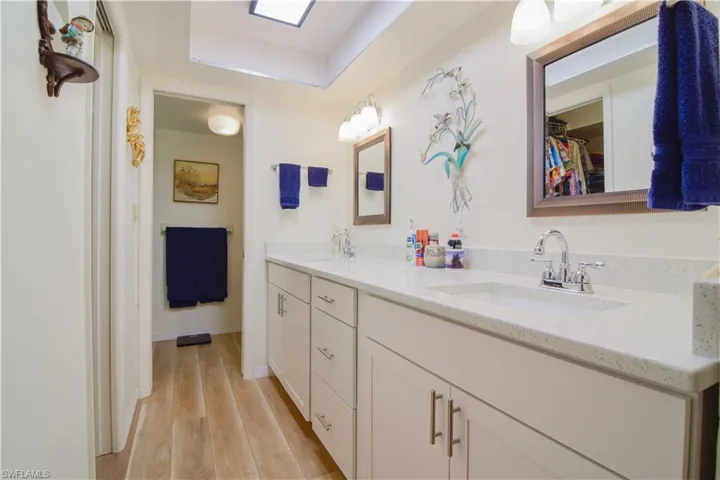 Bathroom featuring a raised ceiling, vanity with extensive cabinet space, wood-type flooring, and double sink