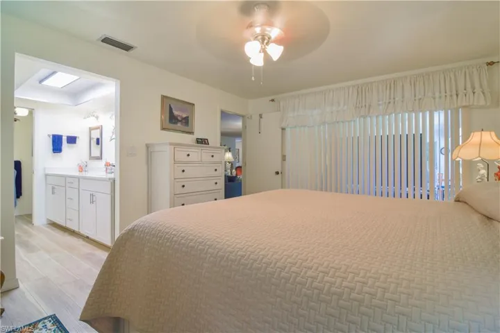 Bedroom with ceiling fan, connected bathroom, a skylight, and light hardwood / wood-style flooring