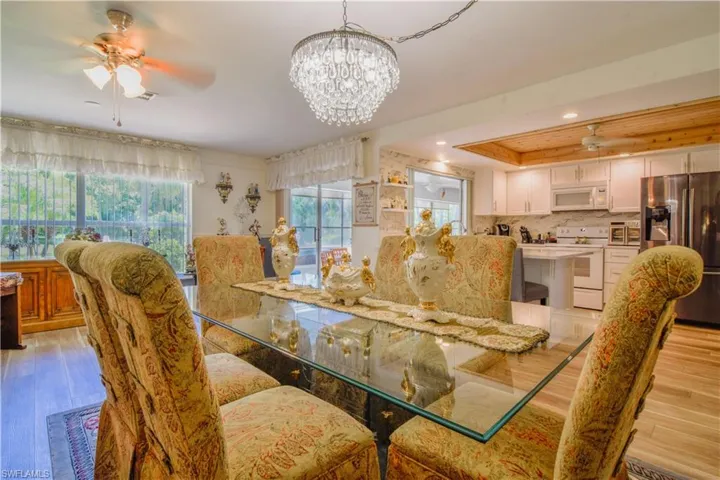 Dining space featuring light hardwood / wood-style floors, a raised ceiling, and ceiling fan with notable chandelier