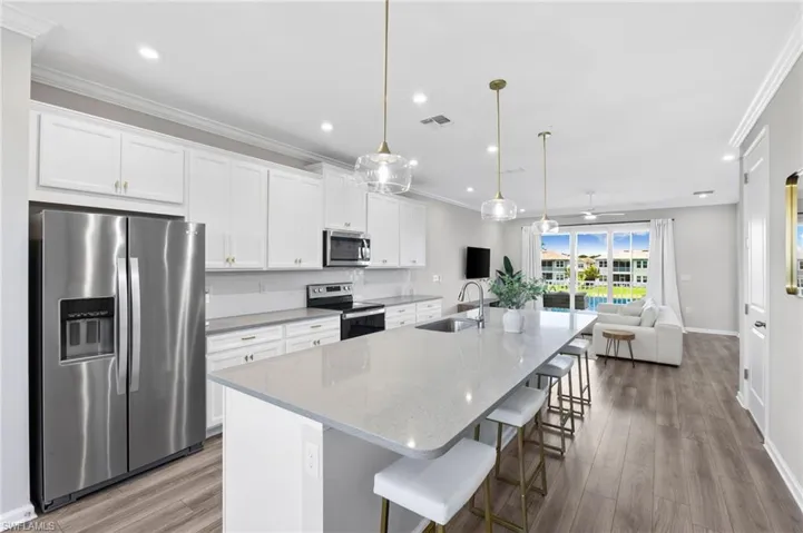 Kitchen featuring appliances with stainless steel finishes, white cabinetry, a breakfast bar area, a large island with sink, and ornamental molding